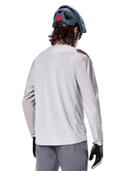 Alpinestars A-Aria Polartec Switch Long Sleeve Jersey, Grigio Chiaro, vista dal retro su un pilota, indossata con casco blu da mountain bike e pantaloni grigi, abbigliamento tecnico da mountain bike per percorsi off-road