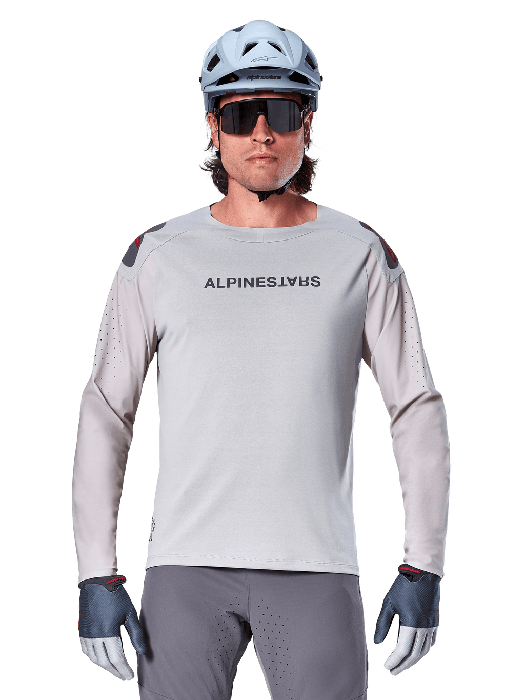 Alpinestars A-Aria Polartec Switch Long Sleeve Jersey, maglia da mountain bike grigio chiaro con perforazioni laser sulle maniche e logo sul petto, indossata con casco celeste, occhiali da sole e guanti grigi