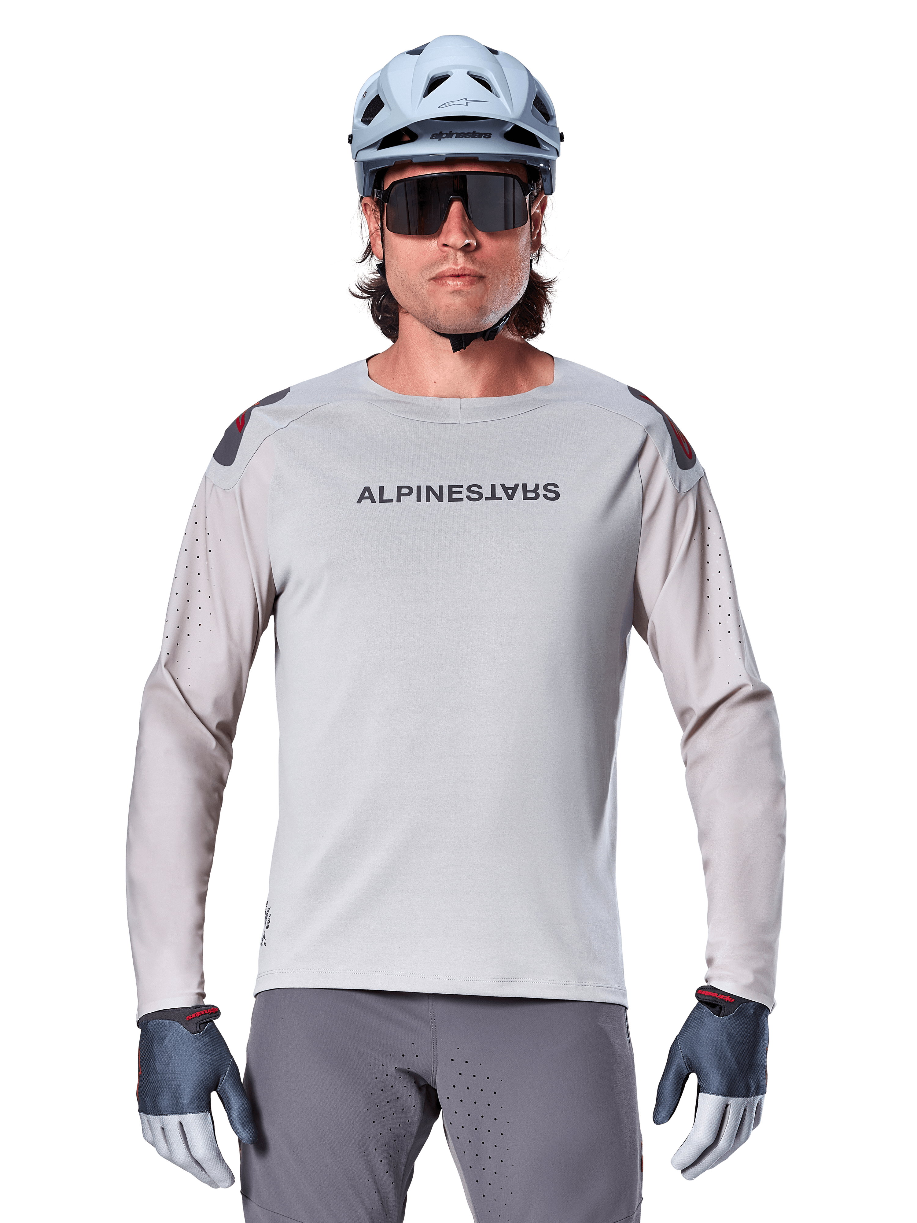 Alpinestars A-Aria Polartec Switch Long Sleeve Jersey, maglia da mountain bike grigio chiaro con perforazioni laser sulle maniche e logo sul petto, indossata con casco celeste, occhiali da sole e guanti grigi