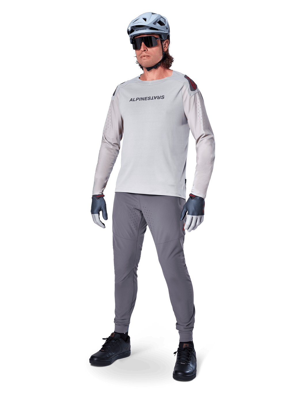 Alpinestars A-Aria Polartec Switch Jersey, maglia da MTB a maniche lunghe, grigio chiaro, indossata con pantaloni da mountain bike grigio scuro, casco e guanti, con maniche traforate al laser e marchio Alpinestars sul petto.