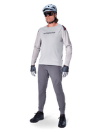 Alpinestars A-Aria Polartec Switch Jersey, maglia da MTB a maniche lunghe, grigio chiaro, indossata con pantaloni da mountain bike grigio scuro, casco e guanti, con maniche traforate al laser e marchio Alpinestars sul petto.
