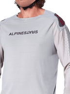 Primo piano della maglia a maniche lunghe Alpinestars A-Aria Polartec Switch in grigio chiaro, con marchio Alpinestars sul petto, logo rosso sulla spalla e maniche traforate al laser per la ventilazione, abbigliamento premium per mountain bike.