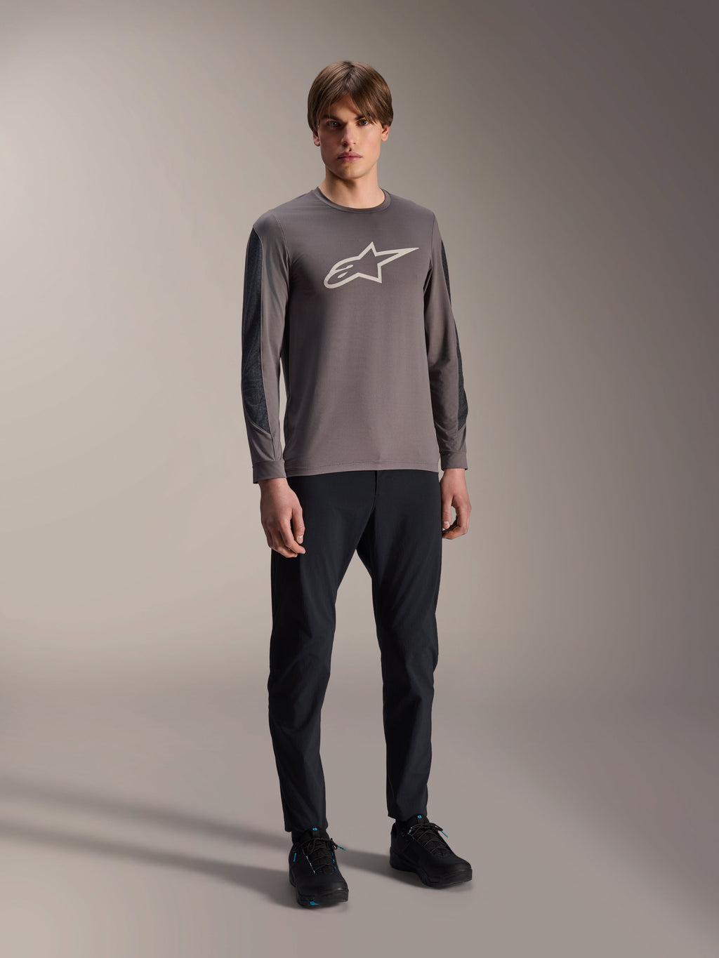 Maglia Alpinestars A-Dura Insert Astar, maglia MTB a maniche lunghe, grigio scuro, con grande logo bianco sul petto, indossata con pantaloni tecnici neri e scarpe nere, abbigliamento per ciclismo off-road