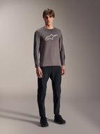 Maglia Alpinestars A-Dura Insert Astar, maglia MTB a maniche lunghe, grigio scuro, con grande logo bianco sul petto, indossata con pantaloni tecnici neri e scarpe nere, abbigliamento per ciclismo off-road