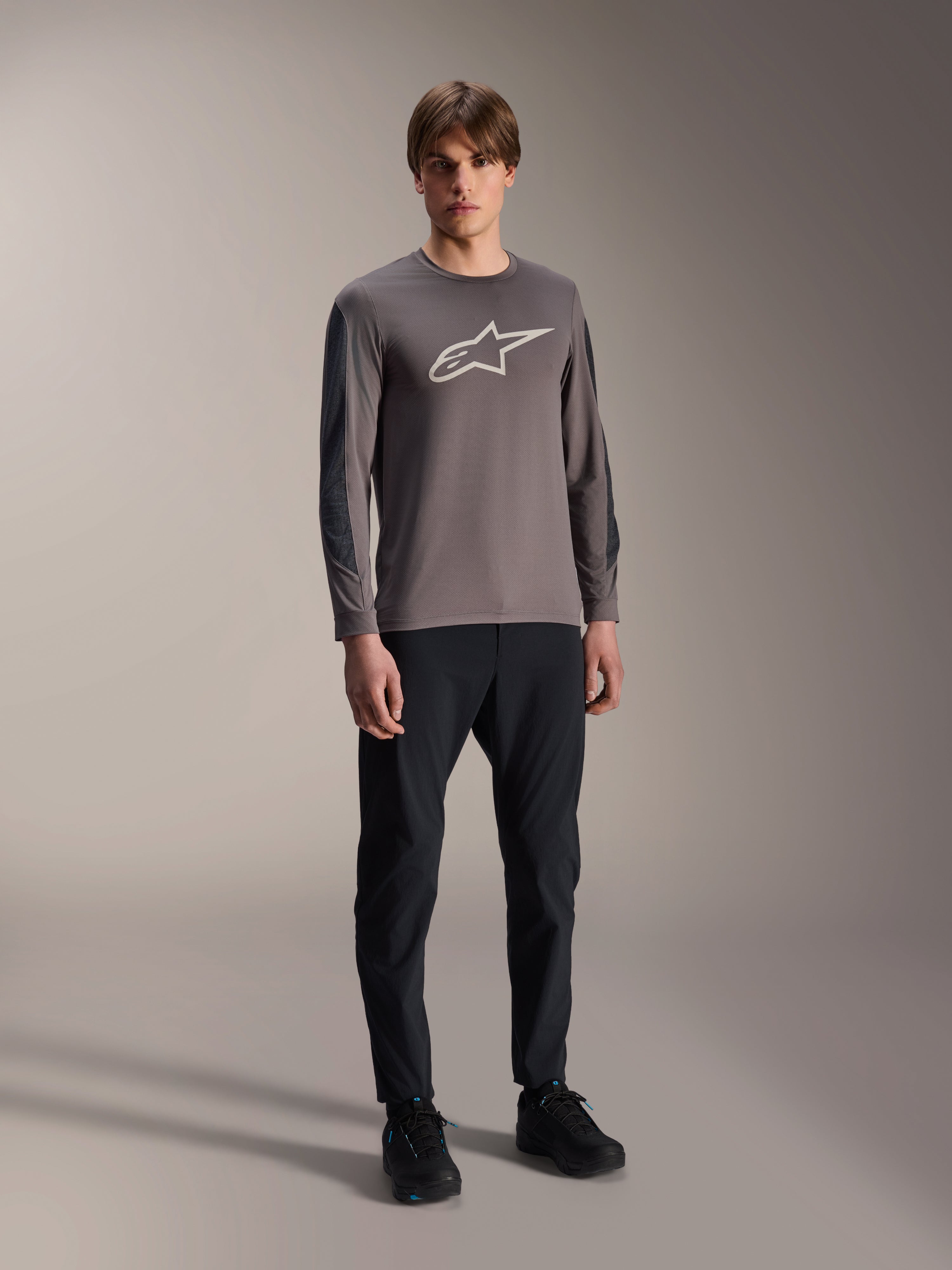 Maglia Alpinestars A-Dura Insert Astar, maglia MTB a maniche lunghe, grigio scuro, con grande logo bianco sul petto, indossata con pantaloni tecnici neri e scarpe nere, abbigliamento per ciclismo off-road