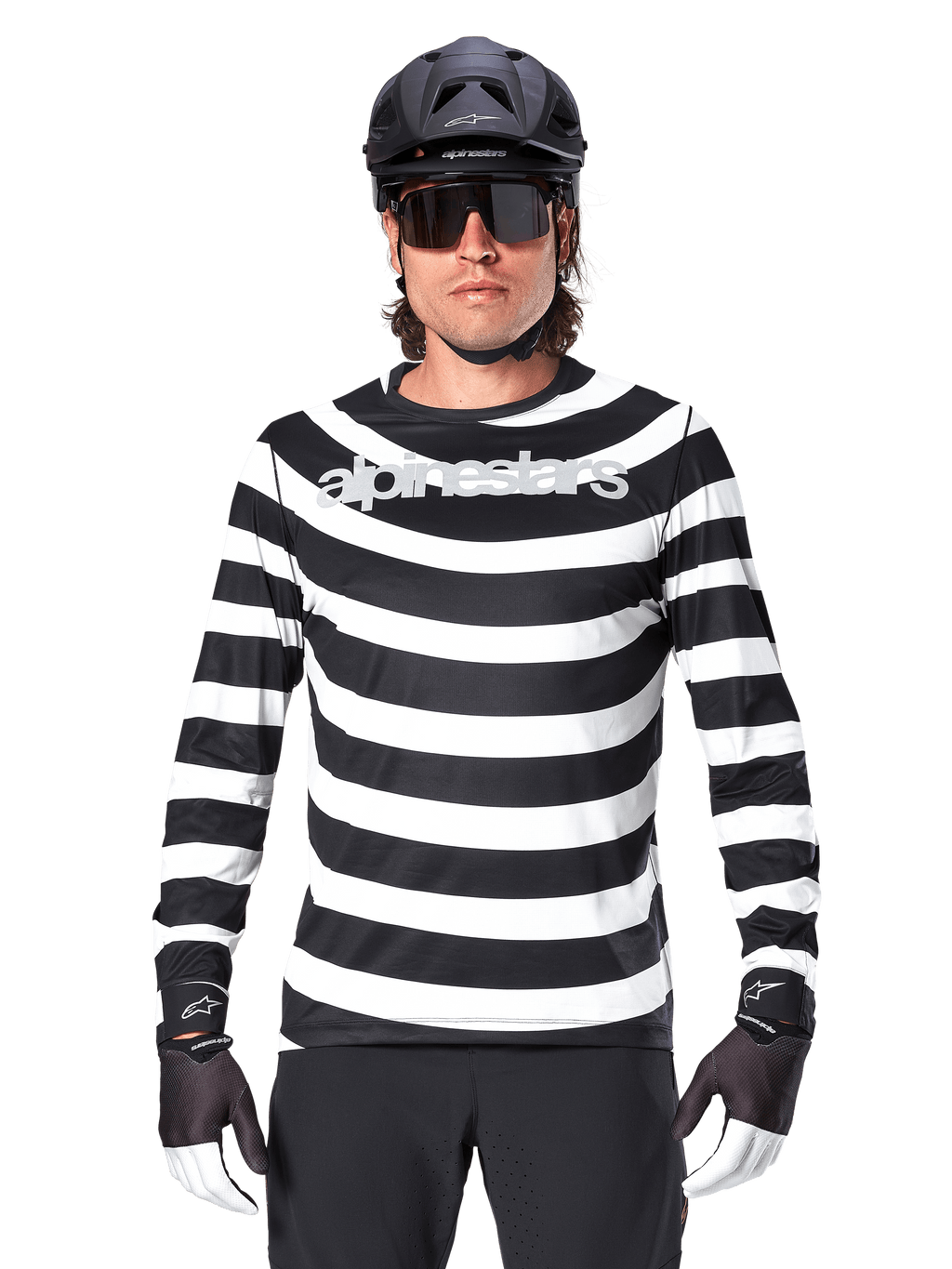 Ciclista uomo con maglia a maniche lunghe Alpinestars A-Aria Oscar, strisce orizzontali bianche e nere, logo Alpinestars riflettente sul petto, abbinata a casco MTB nero, occhiali da ciclismo e guanti tecnici