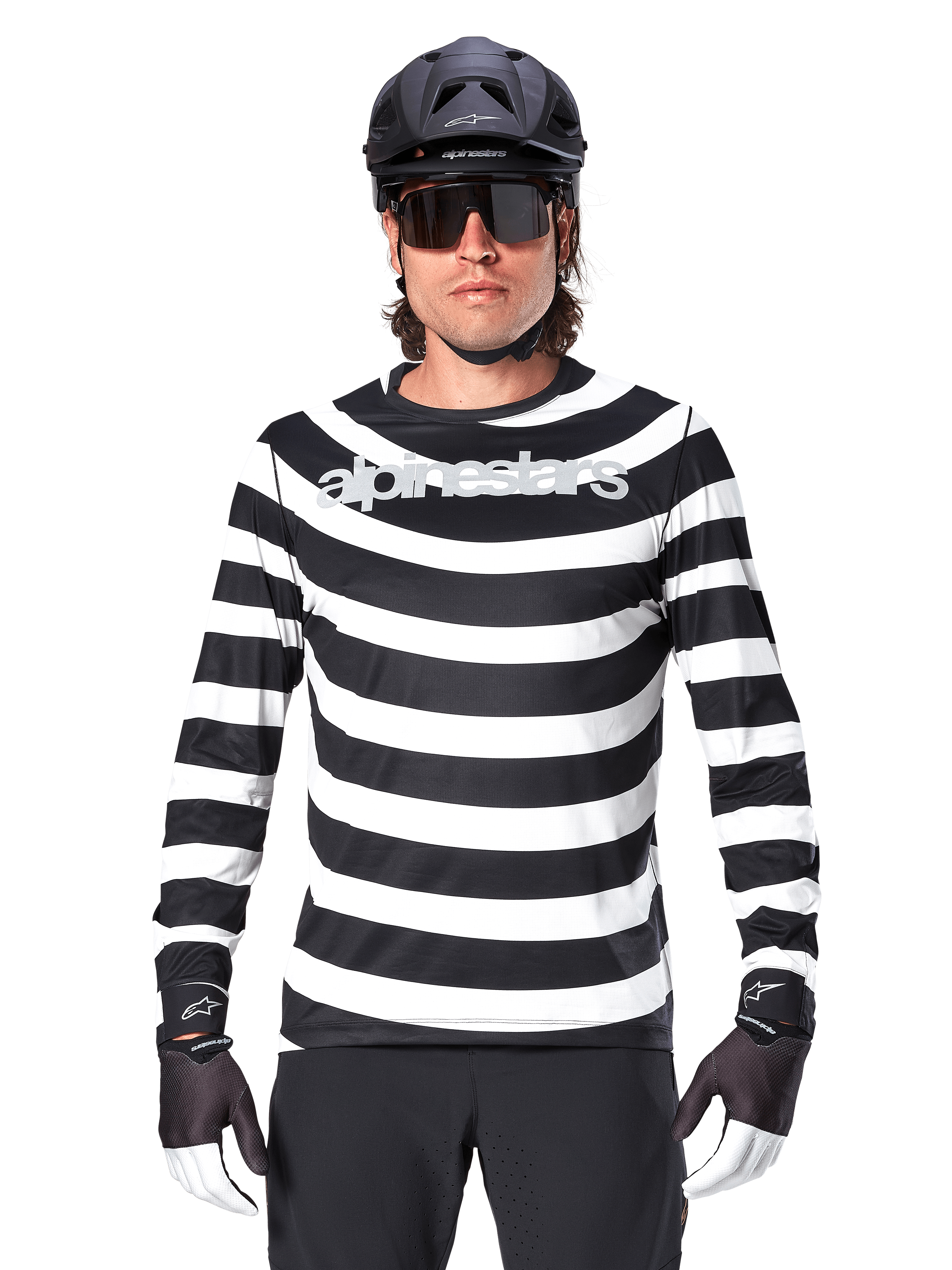 Ciclista uomo con maglia a maniche lunghe Alpinestars A-Aria Oscar, strisce orizzontali bianche e nere, logo Alpinestars riflettente sul petto, abbinata a casco MTB nero, occhiali da ciclismo e guanti tecnici