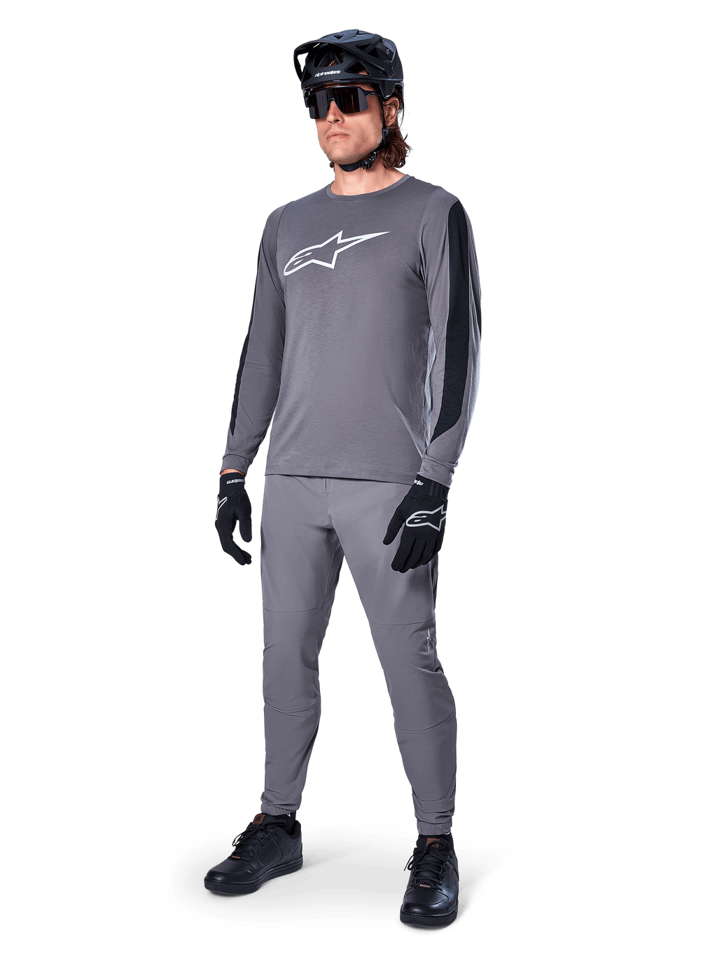 Maglia Alpinestars A-Dura Dri Astar, maglia MTB a maniche lunghe, grigio scuro con logo bianco sul petto, pannelli in mesh neri sulle maniche, indossata con pantaloni grigi coordinati, casco e guanti neri, abbigliamento per mountain bike ad alte prestazioni
