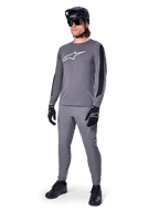 Maglia Alpinestars A-Dura Dri Astar, maglia MTB a maniche lunghe, grigio scuro con logo bianco sul petto, pannelli in mesh neri sulle maniche, indossata con pantaloni grigi coordinati, casco e guanti neri, abbigliamento per mountain bike ad alte prestazioni