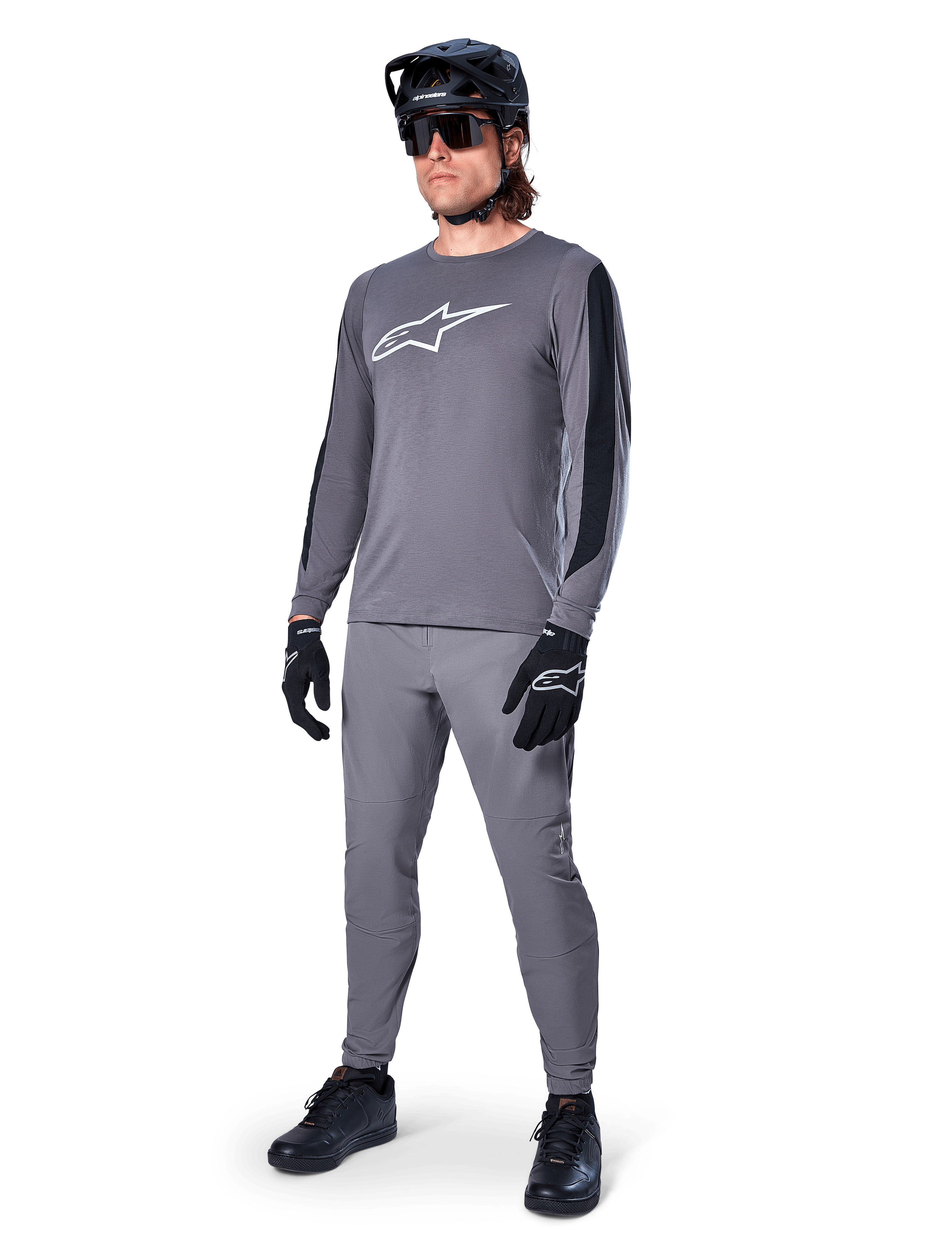 Maglia Alpinestars A-Dura Dri Astar, maglia MTB a maniche lunghe, grigio scuro con logo bianco sul petto, pannelli in mesh neri sulle maniche, indossata con pantaloni grigi coordinati, casco e guanti neri, abbigliamento per mountain bike ad alte prestazioni