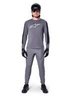 Alpinestars A-Dura Dri Astar Jersey, maglia da MTB a maniche lunghe in grigio scuro, caratterizzata da logo bianco sul petto e pannelli neri sulle maniche, indossata con pantaloni grigi coordinati, casco nero, occhiali da sole e guanti per un outfit completo da ciclismo fuoristrada