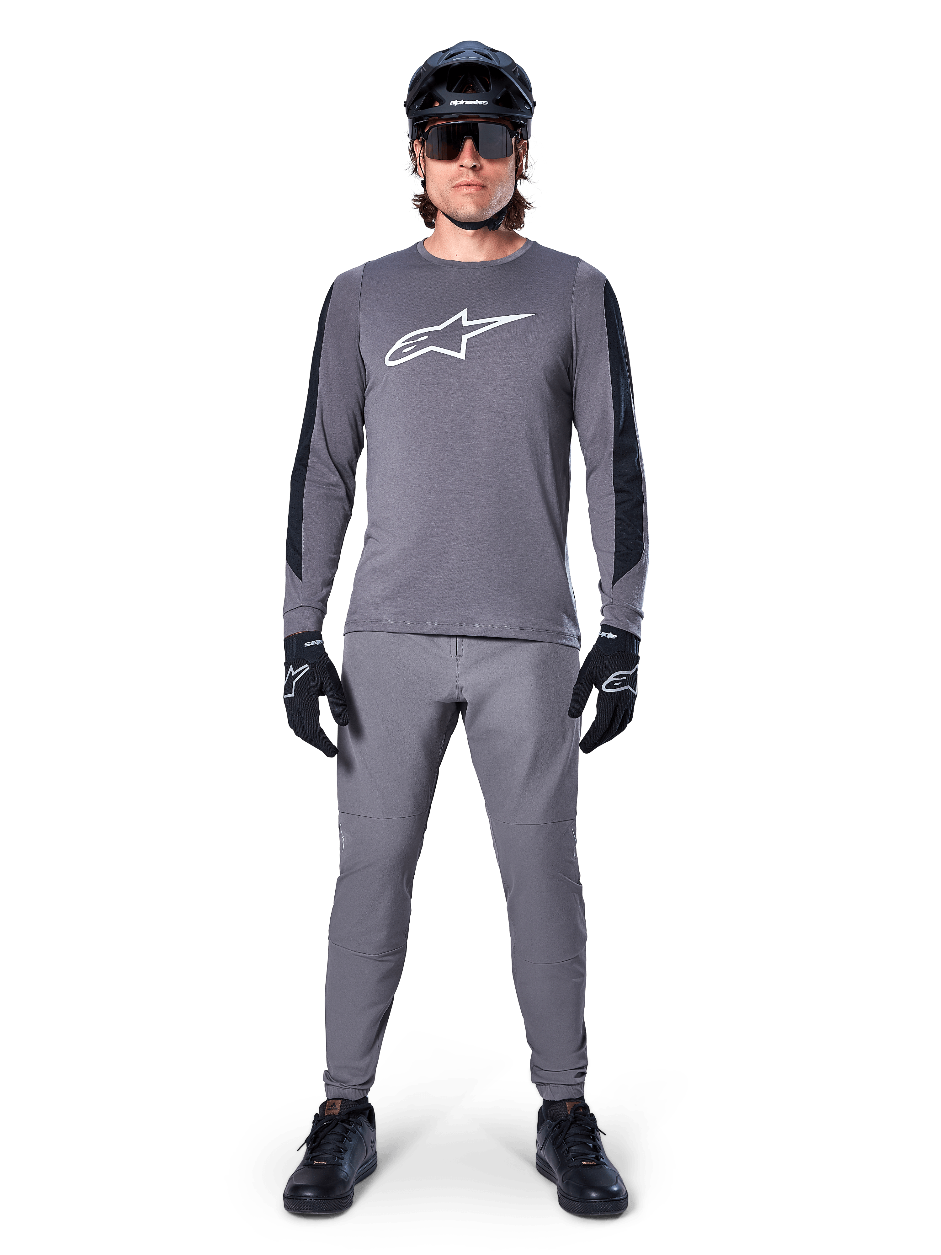 Alpinestars A-Dura Dri Astar Jersey, maglia da MTB a maniche lunghe in grigio scuro, caratterizzata da logo bianco sul petto e pannelli neri sulle maniche, indossata con pantaloni grigi coordinati, casco nero, occhiali da sole e guanti per un outfit completo da ciclismo fuoristrada