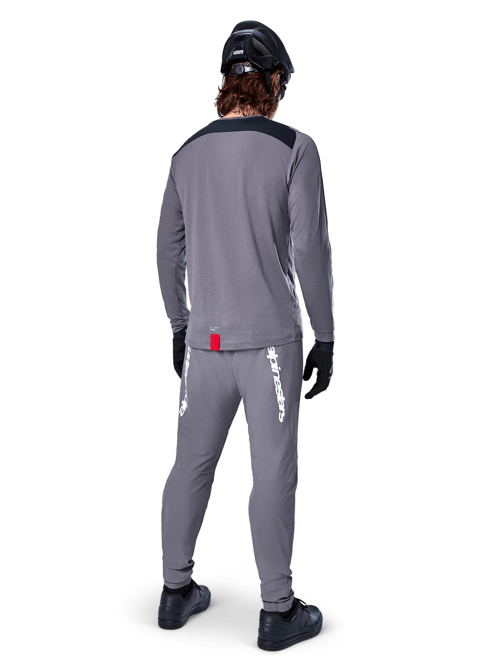 Maglia Alpinestars A-Dura Dri Astar - Maniche Lunghe, grigio scuro, vista posteriore del ciclista con pantaloni abbinati e casco nero, presenta pannelli neri sulle spalle e una piccola etichetta rossa sull'orlo, abbigliamento tecnico da ciclismo fuoristrada