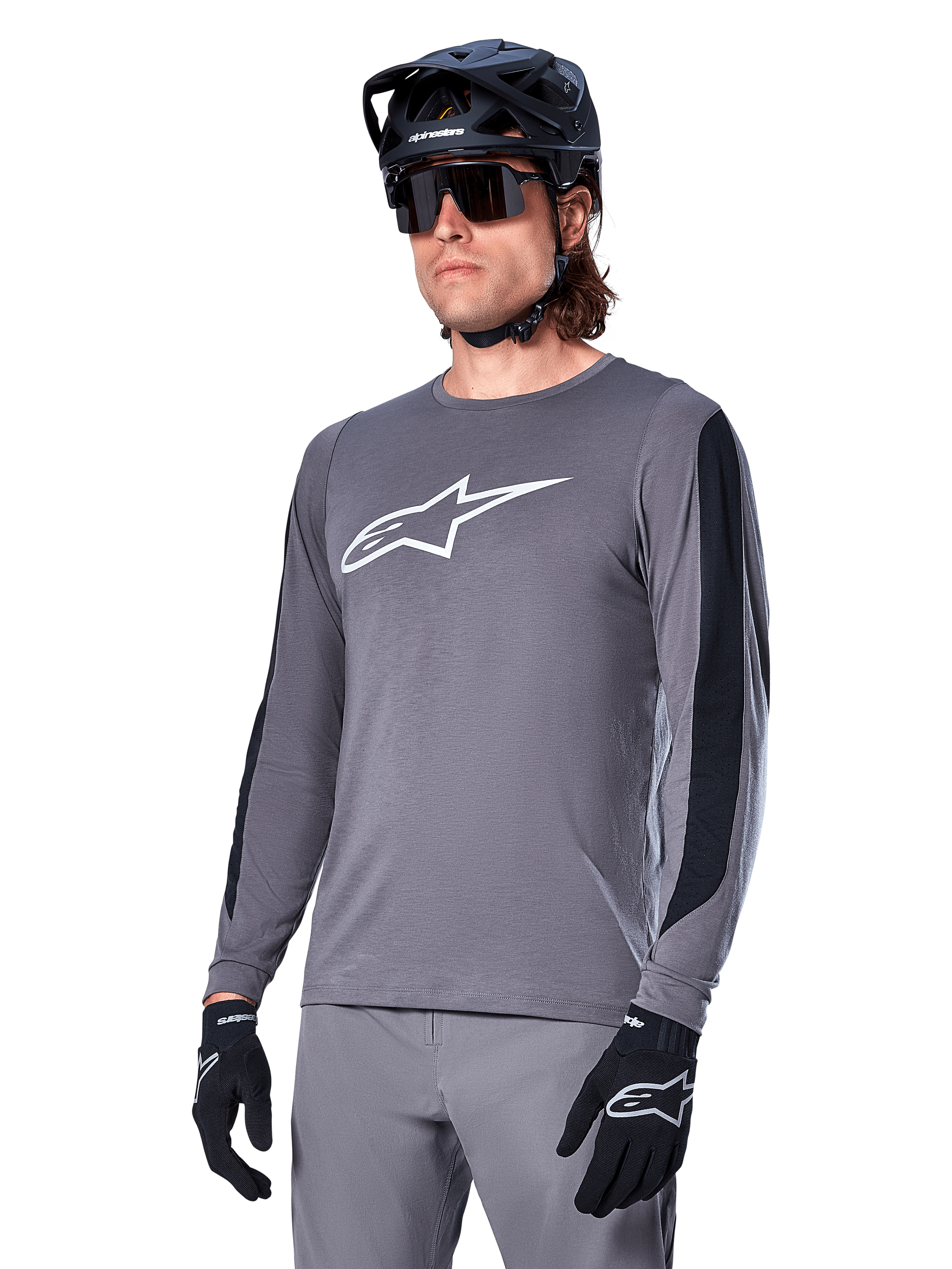 Alpinestars A-Dura Dri Astar Jersey a maniche lunghe, grigio scuro con logo bianco sul petto e pannelli laterali in mesh nero, maglia da mountain bike MTB, indossata con casco nero, occhiali da sole e pantaloni grigi coordinati