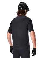Alpinestars A-Aria Polartec Switch Short Sleeve Jersey, nero, vista posteriore su un rider con casco da mountain bike nero, pantaloncini e guanti neri coordinati, abbigliamento tecnico per mountain bike