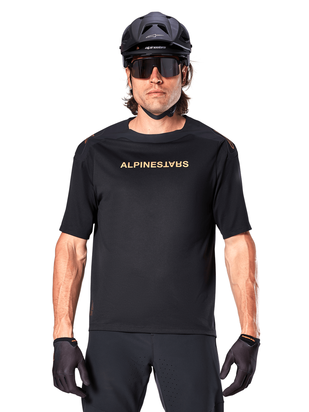 Mountain biker con maglia a maniche corte Alpinestars A-Aria Polartec Switch in nero, logo dorato sul petto, abbinata a casco da MTB nero, occhiali da sole tecnici scuri e guanti coordinati, abbigliamento da ciclismo fuoristrada.