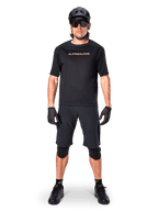 Alpinestars A-Aria Polartec Switch Jersey, maglia MTB a maniche corte, nero con scritte tan, indossata con equipaggiamento da mountain bike nero coordinato comprensivo di casco, pantaloncini e ginocchiere, abbigliamento tecnico da ciclismo fuoristrada