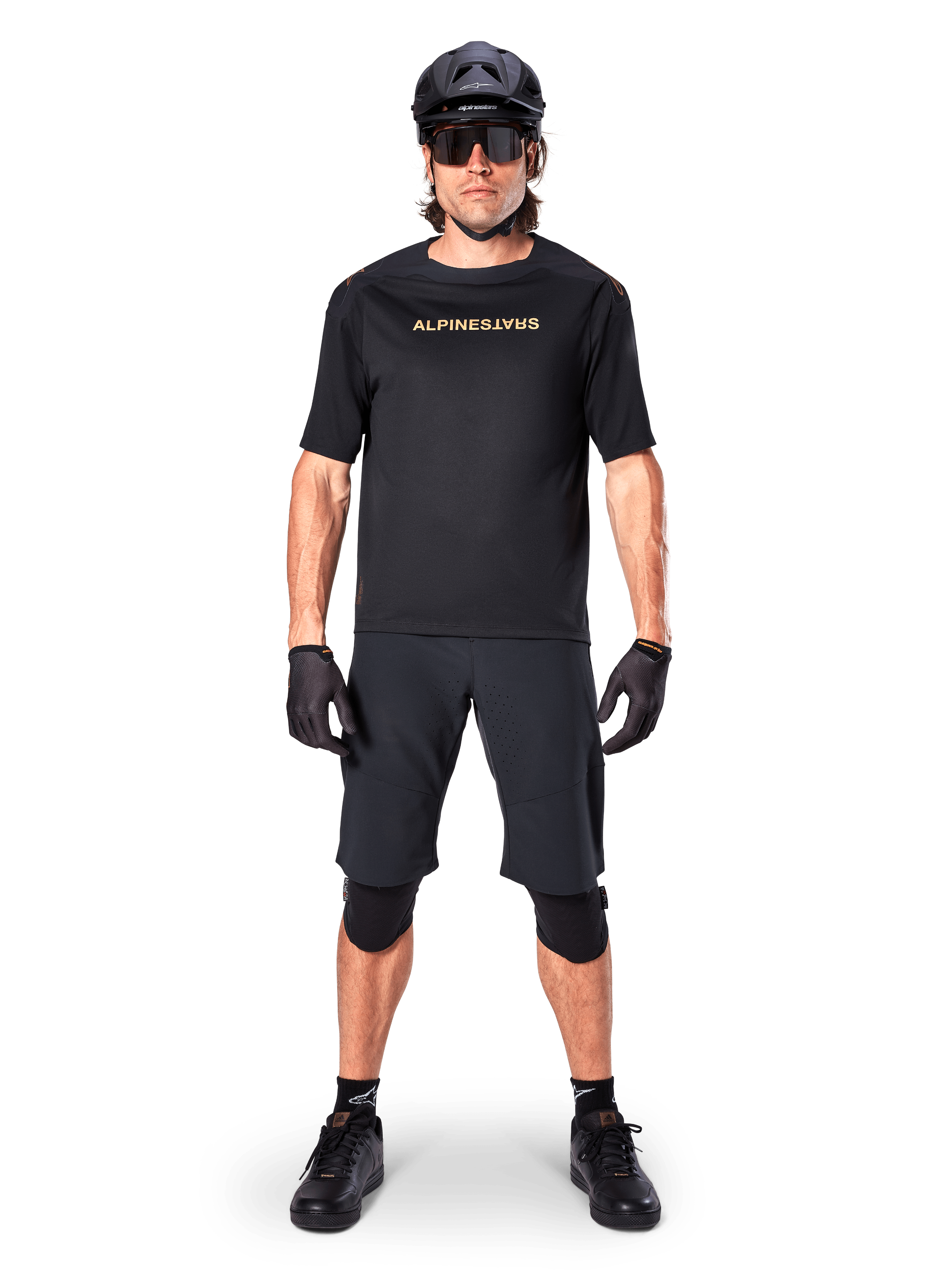 Alpinestars A-Aria Polartec Switch Jersey, maglia MTB a maniche corte, nero con scritte tan, indossata con equipaggiamento da mountain bike nero coordinato comprensivo di casco, pantaloncini e ginocchiere, abbigliamento tecnico da ciclismo fuoristrada
