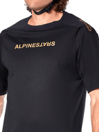 Alpinestars A-Aria Polartec Switch Jersey, maglia MTB a maniche corte, nero, scritta Alpinestars dorata sul petto e logo sulla spalla, primo piano del busto che mette in risalto il tessuto tecnico e la vestibilità performante
