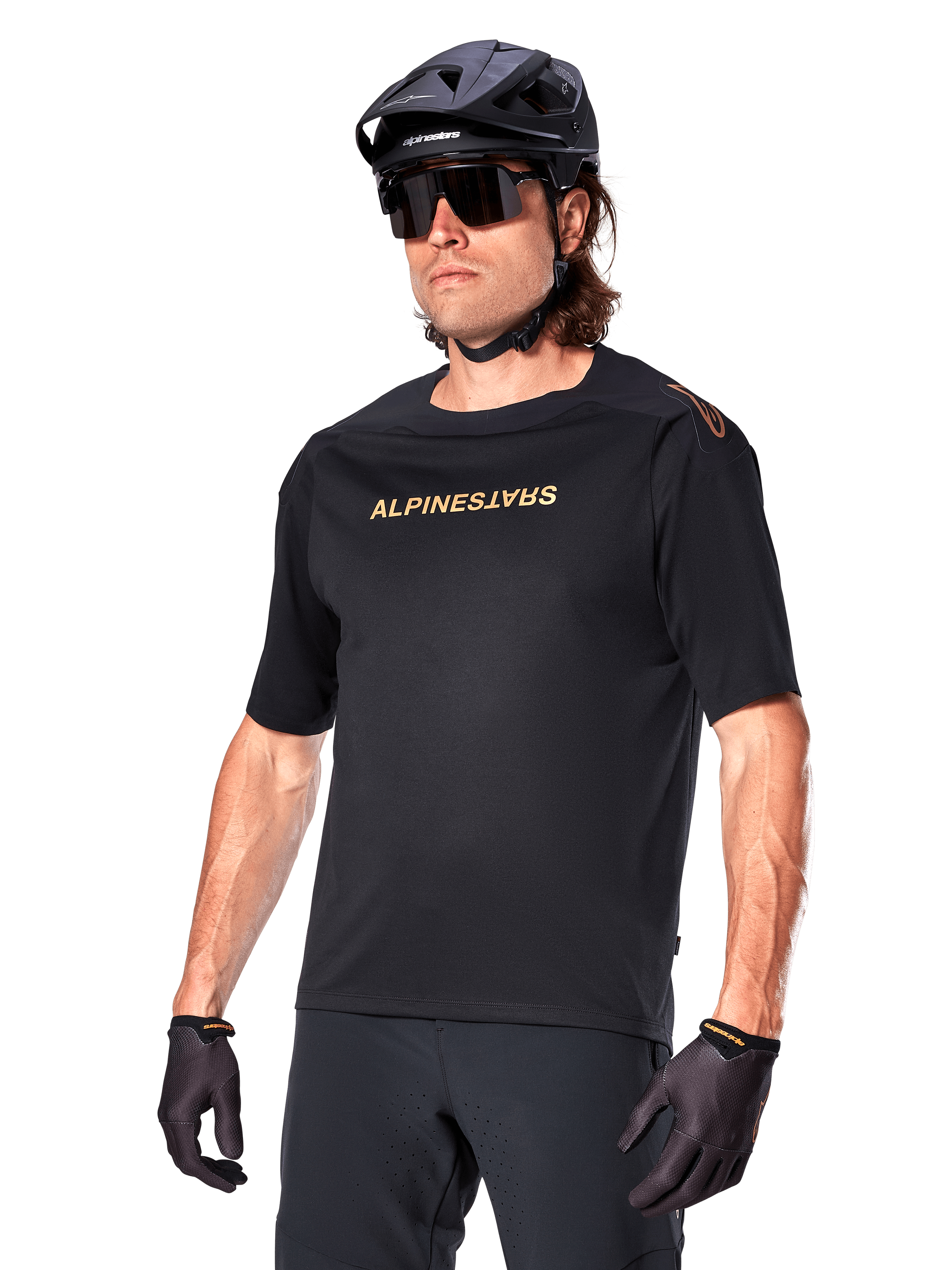 Alpinestars A-Aria Polartec Switch Jersey a maniche corte, maglia da mountain bike nera con logo Alpinestars color oro, indossata con casco nero, occhiali da sole e guanti, abbigliamento tecnico da MTB
