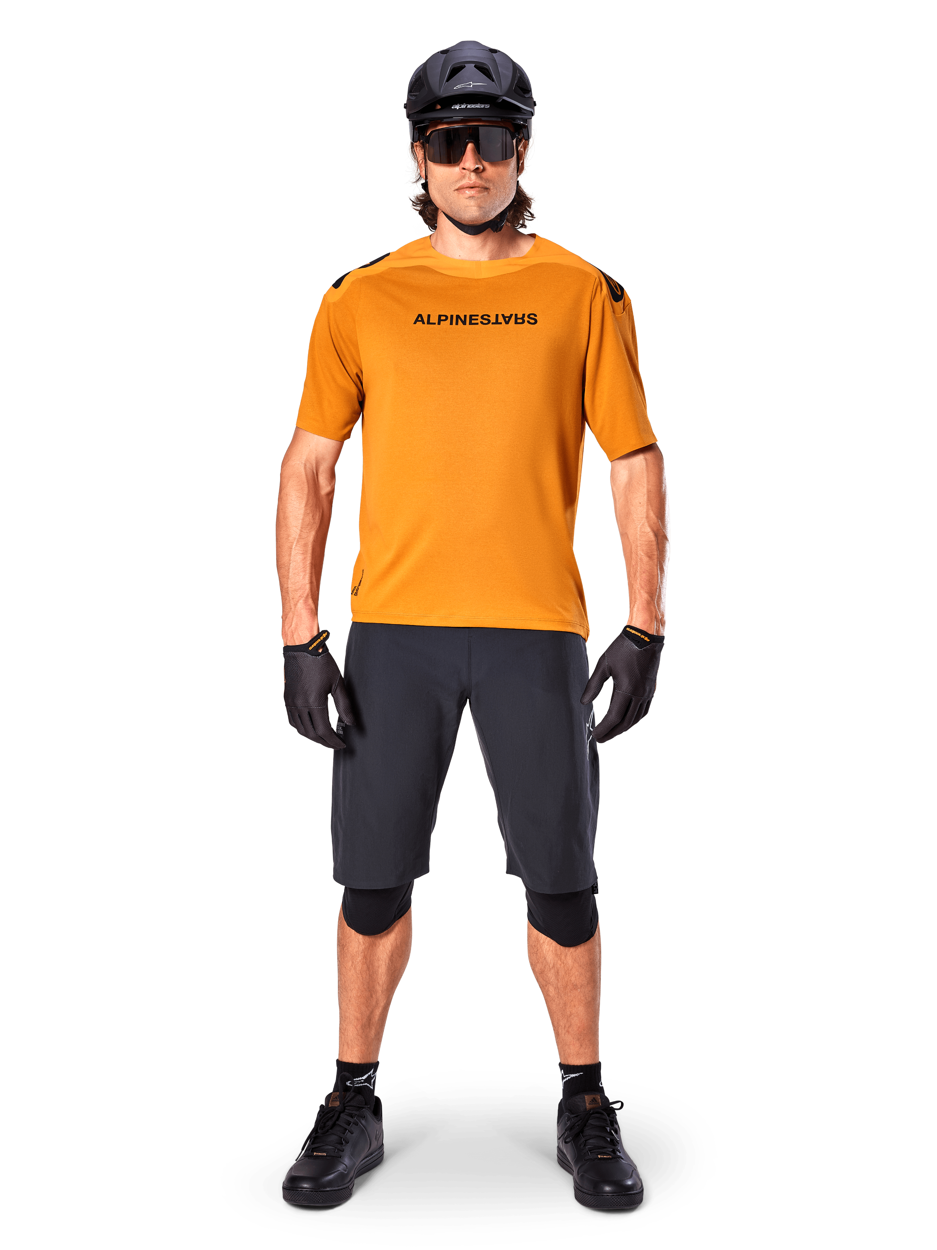 Ciclista uomo che indossa la maglia a maniche corte Alpinestars A-Aria Polartec Switch in Dark Gold, abbinata a pantaloncini da MTB neri, casco, occhiali da sole e guanti, abbigliamento professionale da mountain bike