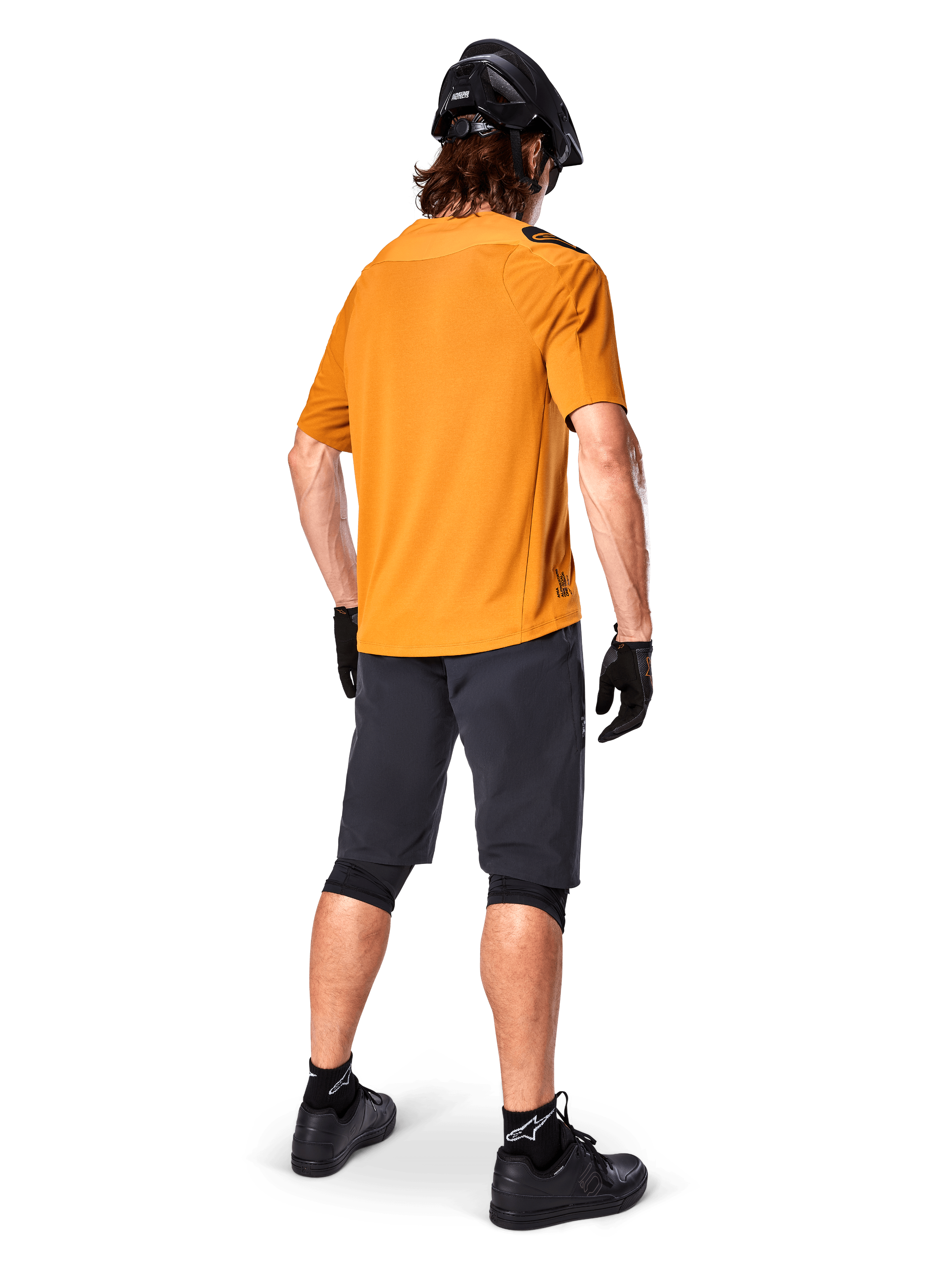 Alpinestars Maglia A-Aria Polartec Switch, maglia MTB a maniche corte, oro scuro, vista posteriore del modello con pantaloncini da mountain bike grigio scuro, casco nero e guanti, abbigliamento tecnico da ciclismo per percorsi fuoristrada