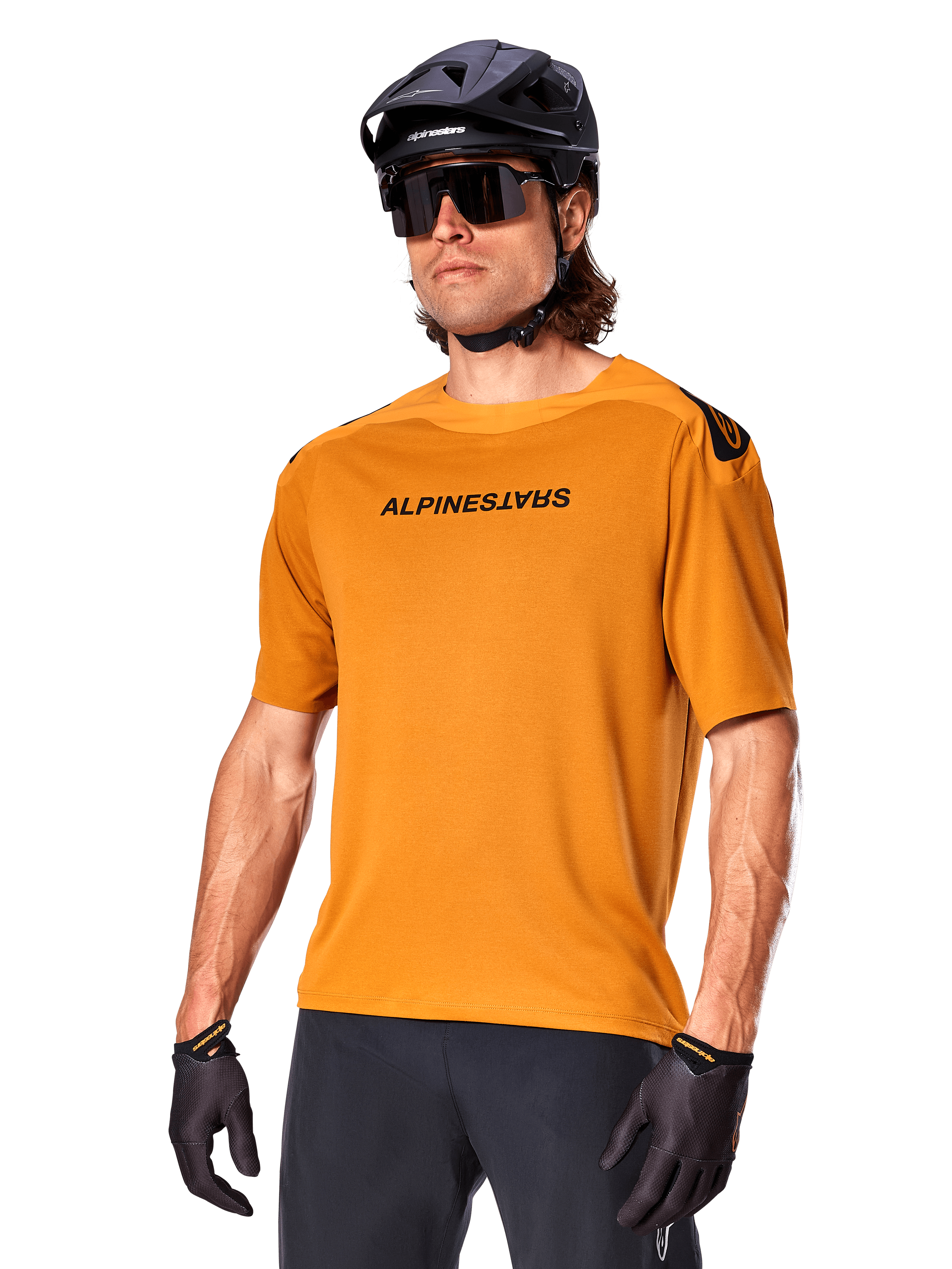 Maglia Alpinestars A-Aria Polartec Switch a maniche corte, color oro scuro con logo nero, indossata da un modello con casco nero, occhiali da sole e guanti da ciclismo, abbigliamento da mountain bike ad alte prestazioni