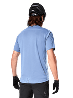 Maglia a maniche corte Alpinestars A-Dura Dri Astar, maglia MTB, Blu Infinity, vista posteriore con pannelli di ventilazione in mesh sulle spalle e coda più lunga, indossata con casco da MTB e guanti neri, abbigliamento tecnico da ciclismo