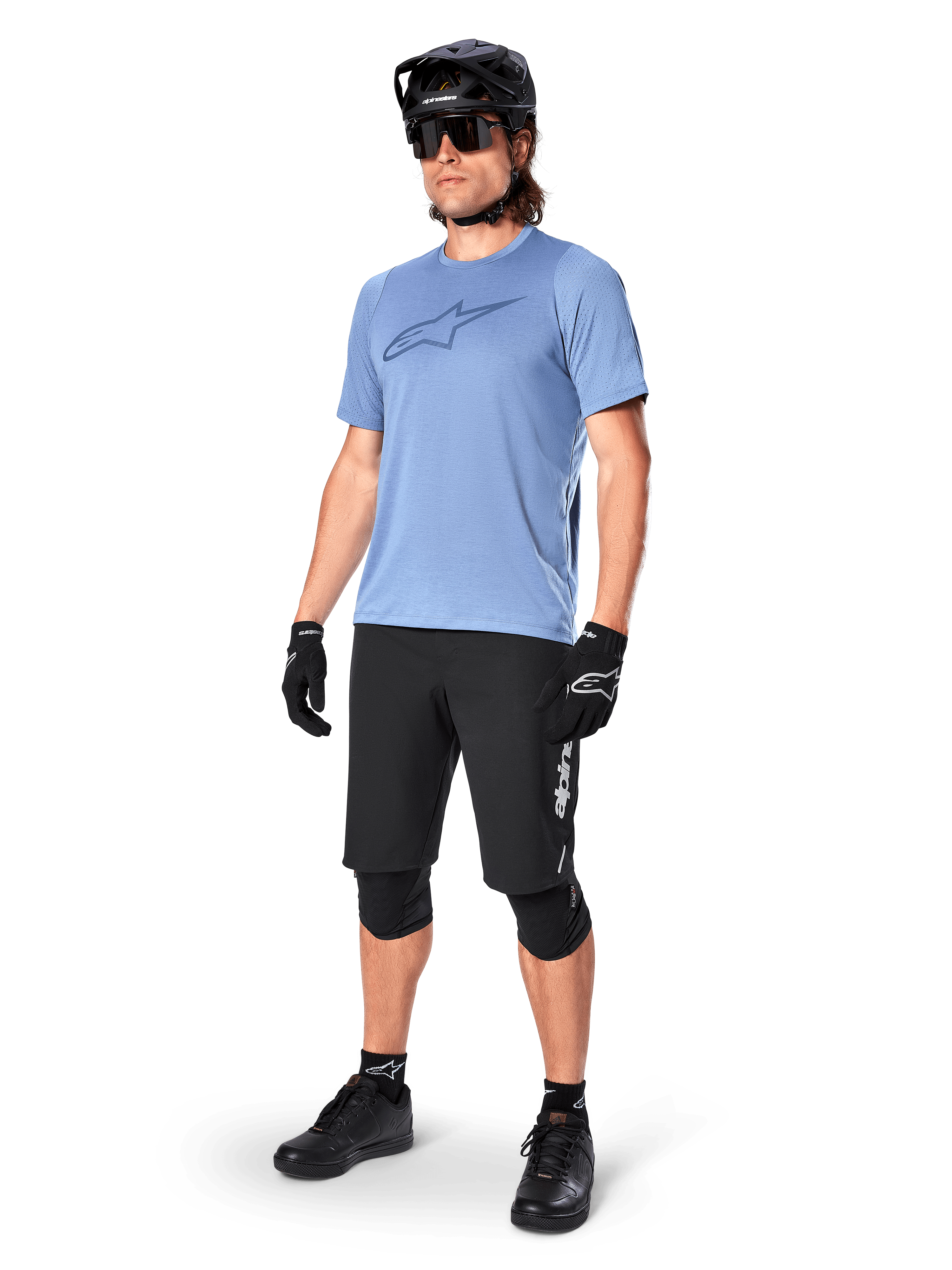 Pilota uomo che indossa la maglia a maniche corte Alpinestars A-Dura Dri Astar in Infinity Blue, abbinata a pantaloncini da MTB neri, casco nero, occhiali da sole, ginocchiere e guanti, outfit completo da mountain bike