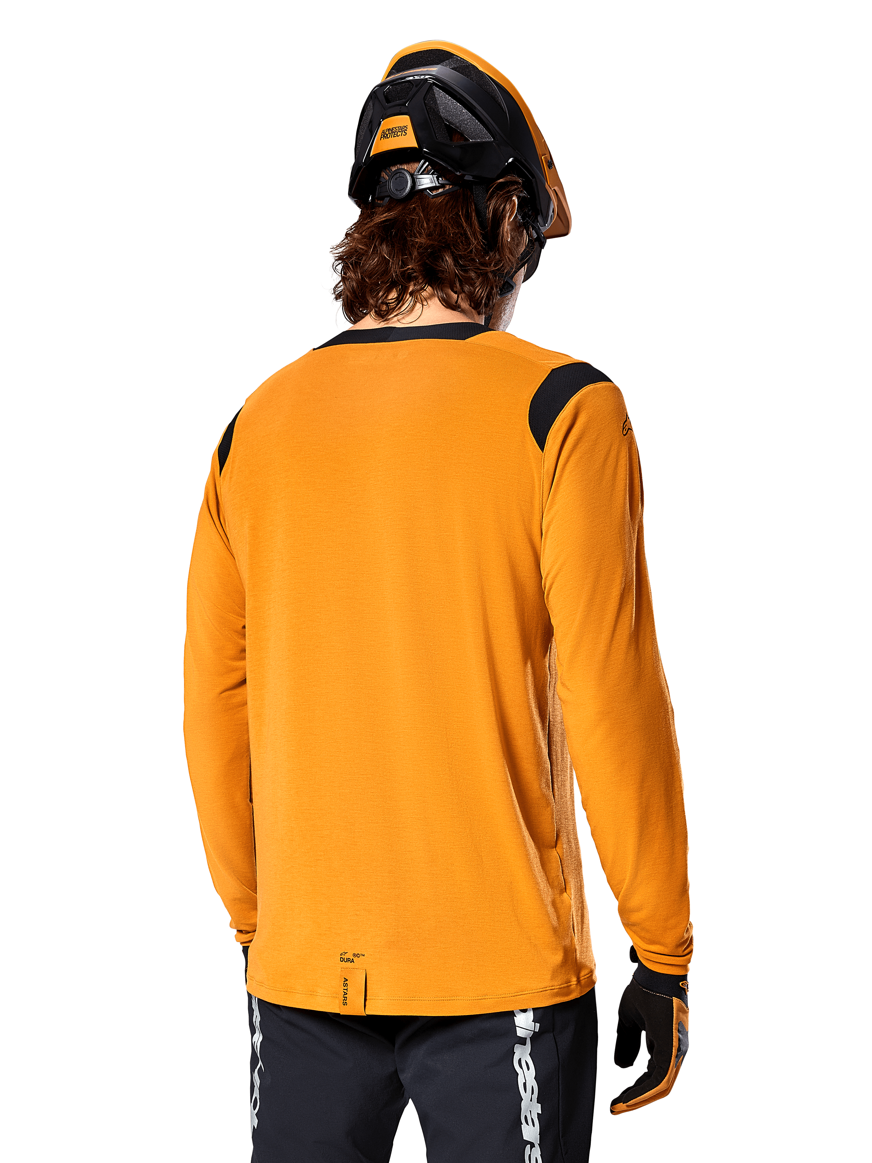 Alpinestars A-Dura Dri Wool Long Sleeve Jersey in Dark Gold, vista posteriore di un ciclista con casco da mountain bike e guanti, con pannelli in rete nera sulle spalle e coda più lunga, abbigliamento tecnico da ciclismo per trail riding