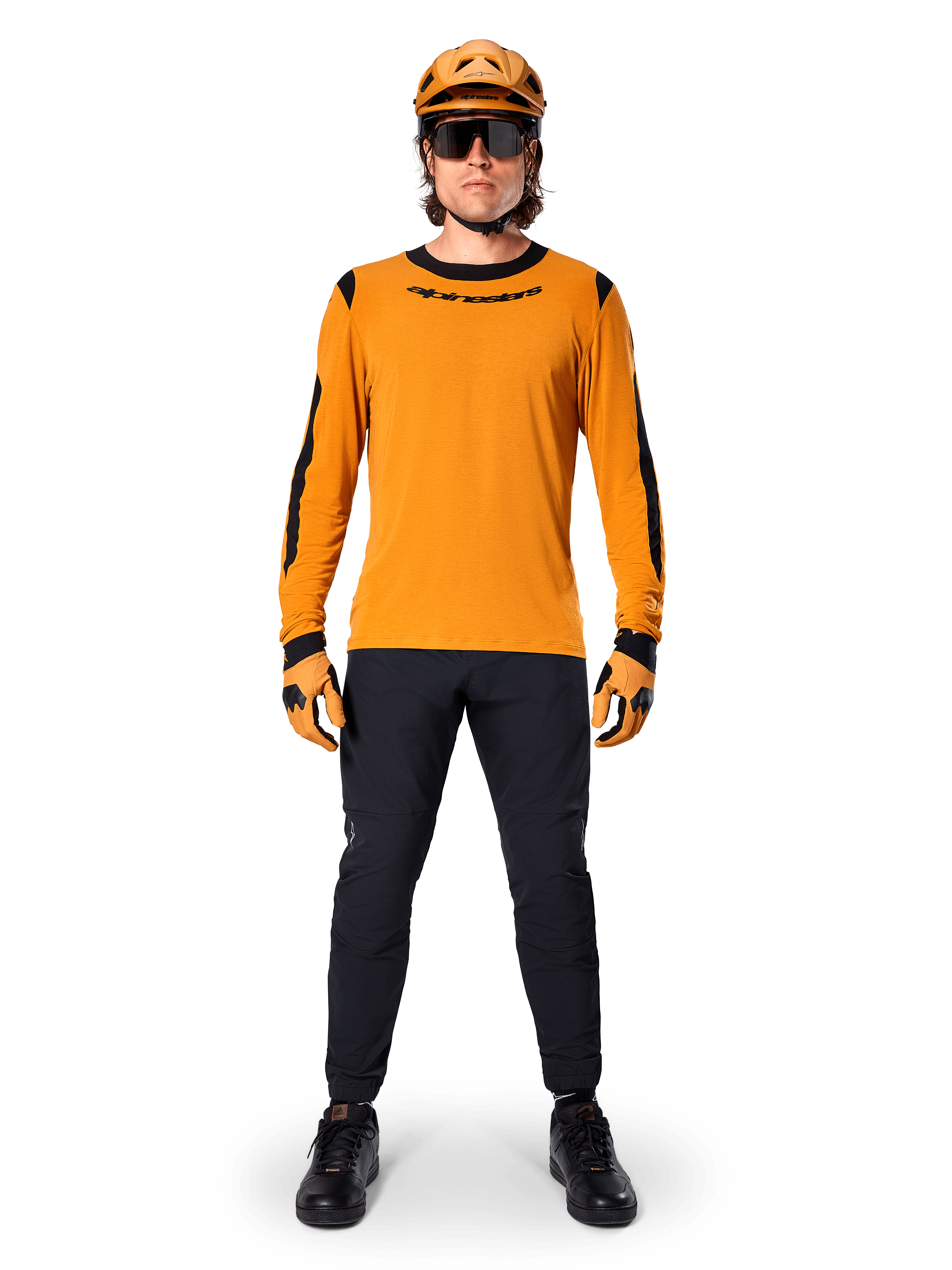Mountain biker con maglia Alpinestars A-Dura Dri Wool a maniche lunghe, oro scuro con accenti neri su collo e maniche, abbinata a pantaloni neri, casco color oro coordinato, guanti e occhiali da sole neri, abbigliamento professionale da mountain bike