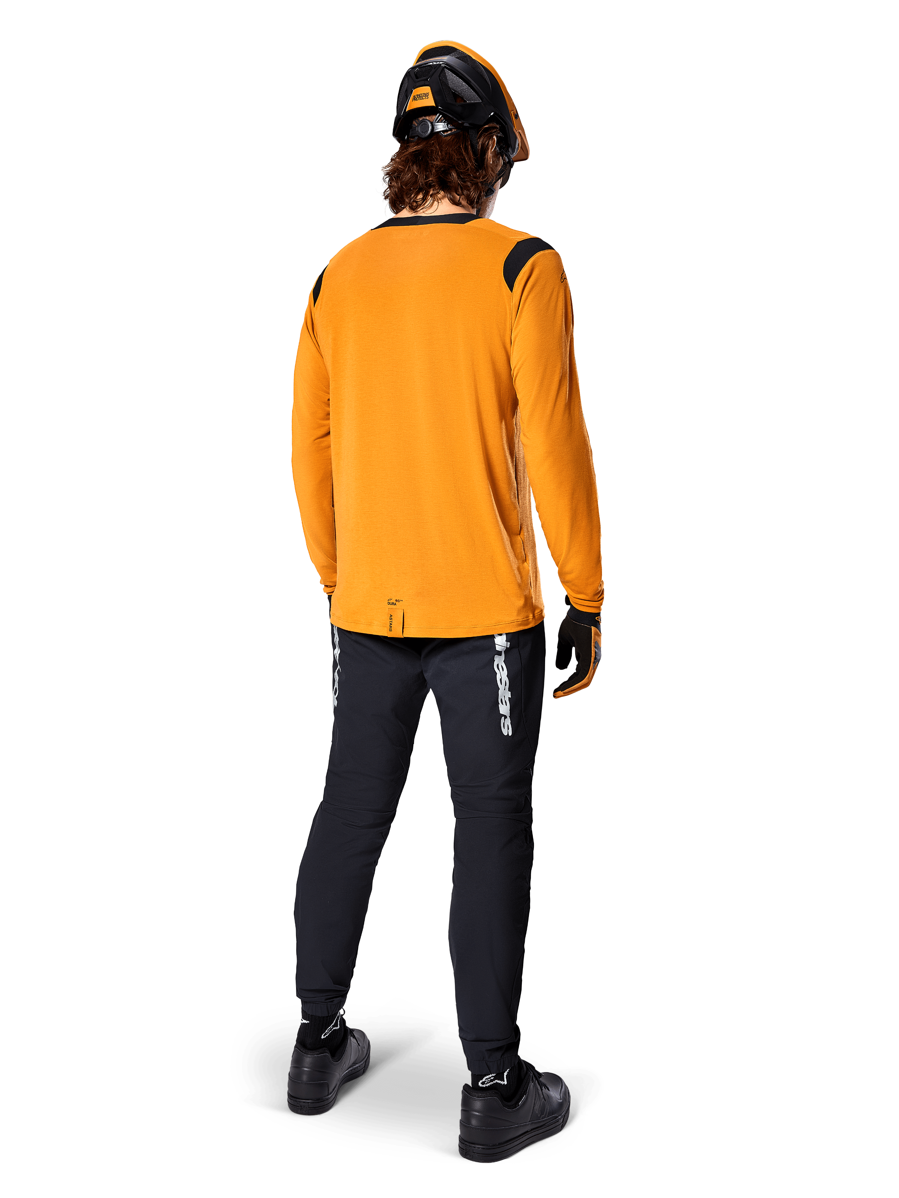 Mountain biker visto da dietro che indossa la maglia Alpinestars A-Dura Dri Wool a maniche lunghe in Dark Gold, pantaloni tecnici neri con logo bianco e un casco coordinato nero e arancione, abbigliamento da mountain bike ad alte prestazioni.