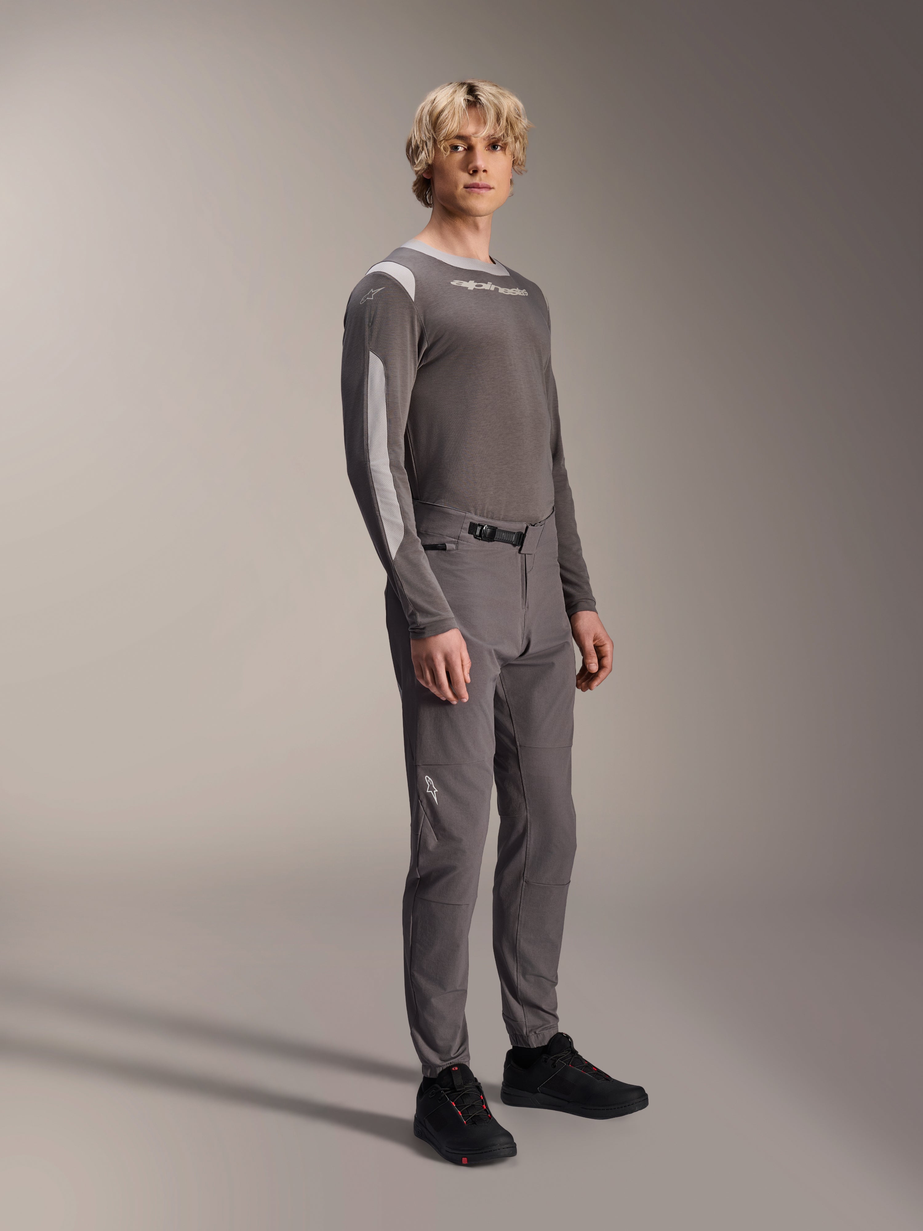 Alpinestars A-Dura Elite Pants, pantaloni da mountain bike, grigio scuro, indossati con maglia coordinata a maniche lunghe e scarpe nere, dotati di chiusura anteriore a cricchetto e tessuto Cordura resistente per trail ed enduro