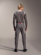 Modello visto da dietro che indossa pantaloni Alpinestars A-Dura Elite grigio scuro e una maglia grigia coordinata a maniche lunghe, con loghi Alpinestars bianchi sulle gambe, dettaglio rosso in vita e scarpe nere, abbigliamento professionale da MTB.