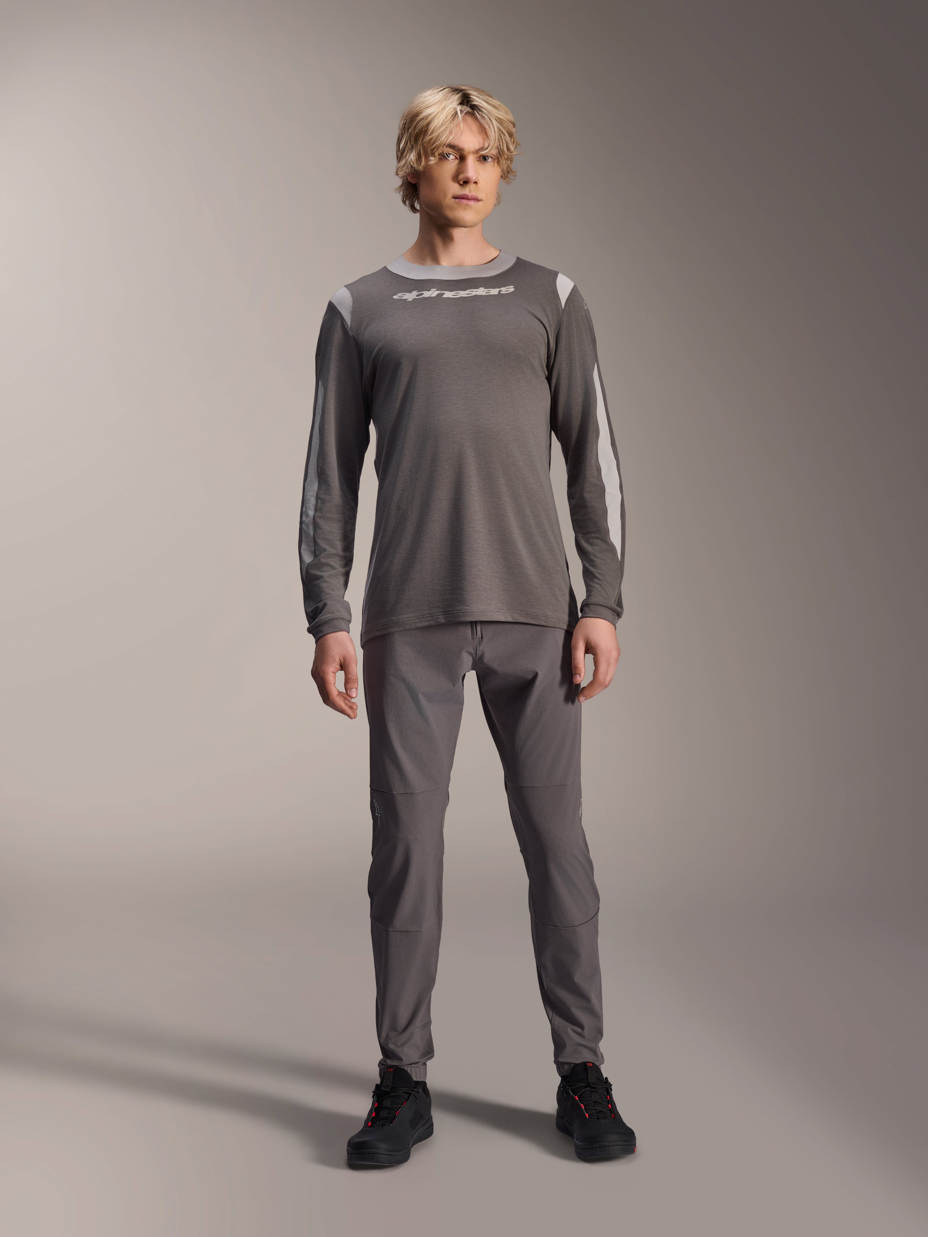 Maglia a maniche lunghe Alpinestars A-Dura Dri Wool, grigio scuro, indossata da un modello con pantaloni grigi coordinati e scarpe nere, logo Alpinestars bianco sul petto, pannelli in rete grigio chiaro su spalle e maniche, abbigliamento tecnico per mountain bike