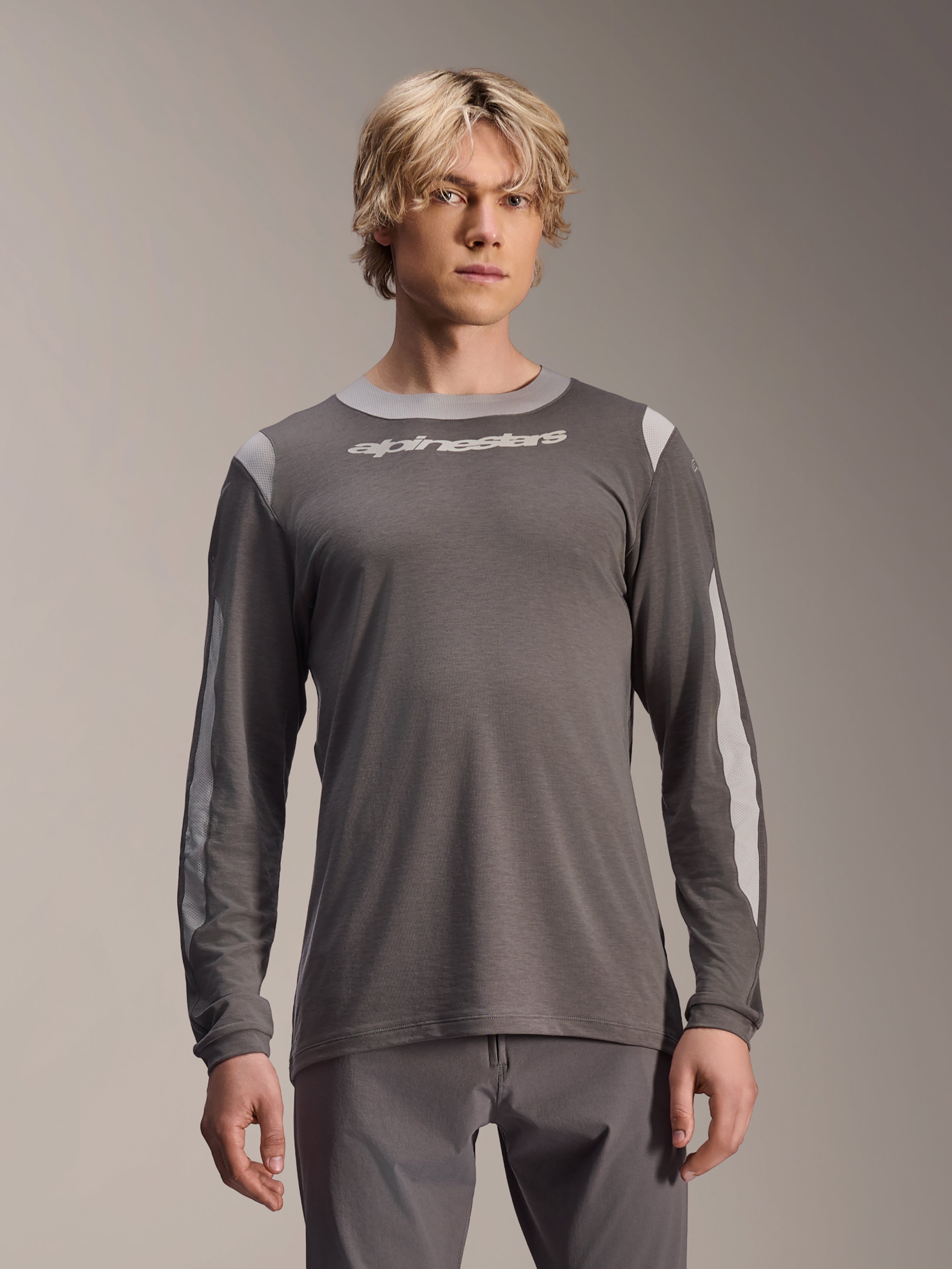 Alpinestars A-Dura Dri Wool Jersey a maniche lunghe, grigio scuro, indossata da un modello, con pannelli in rete grigio chiaro su spalle e maniche, logo bianco sul petto, abbigliamento tecnico per mountain bike