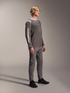 Modello con maglia Alpinestars A-Dura Dri Wool a maniche lunghe in grigio scuro, pantaloni grigi coordinati e scarpe nere, con pannelli in rete grigio chiaro su spalle e maniche, abbigliamento tecnico da MTB per il ciclismo fuoristrada