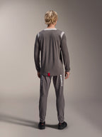 Maglia Alpinestars A-Dura Dri Wool a maniche lunghe, grigio scuro, vista posteriore su modello, con pannelli in rete grigio chiaro su spalle e colletto, bordo posteriore più lungo con piccola etichetta rossa del brand, indossata con pantaloni da ciclismo grigi coordinati
