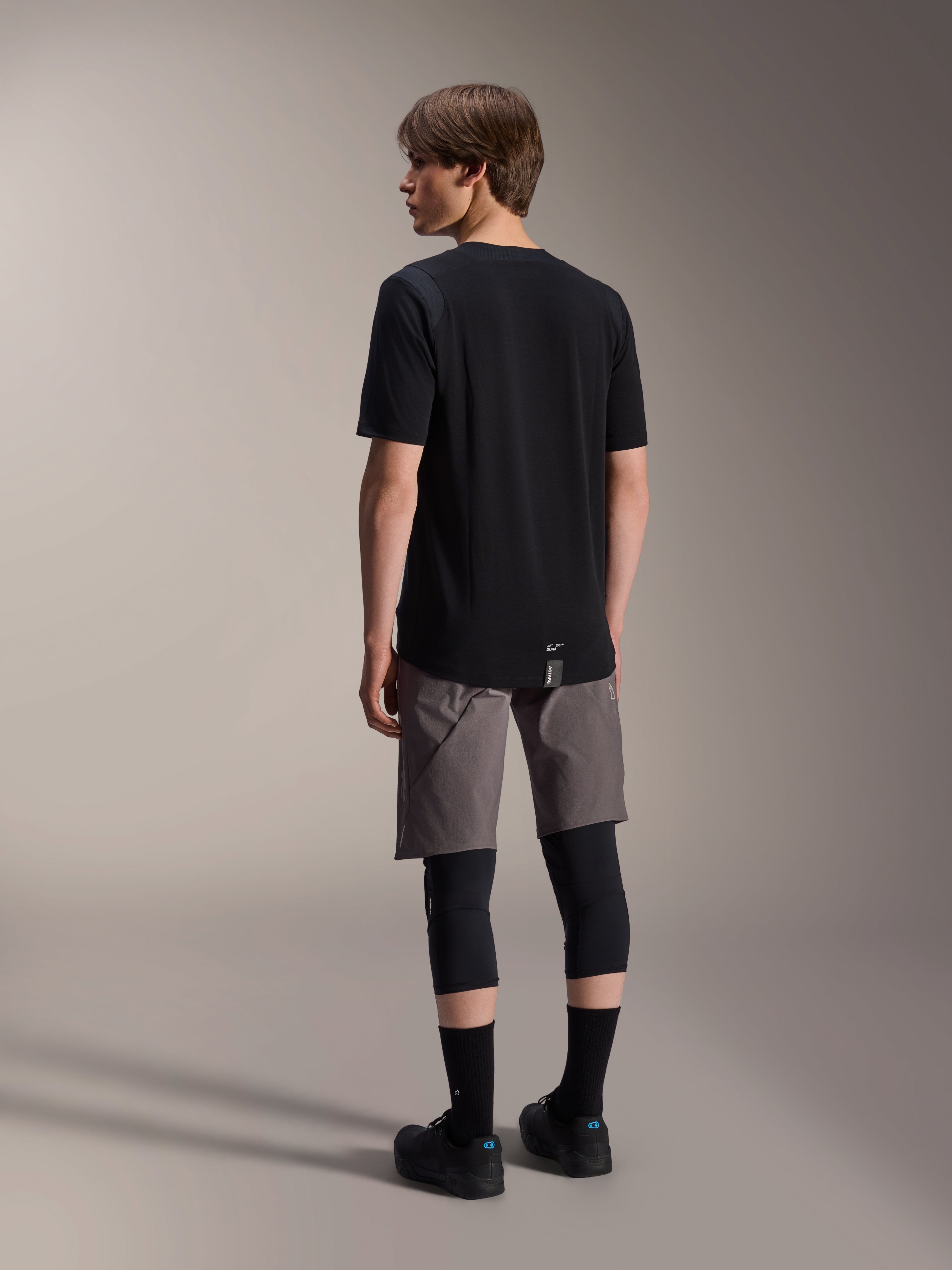 Maglia a maniche corte Alpinestars A-Dura Dri Wool e pantaloncini A-Dura Elite, abbigliamento da mountain bike nero e grigio scuro, indossati con ginocchiere e calze nere, vista posteriore dell'abbigliamento tecnico per prestazioni off-road