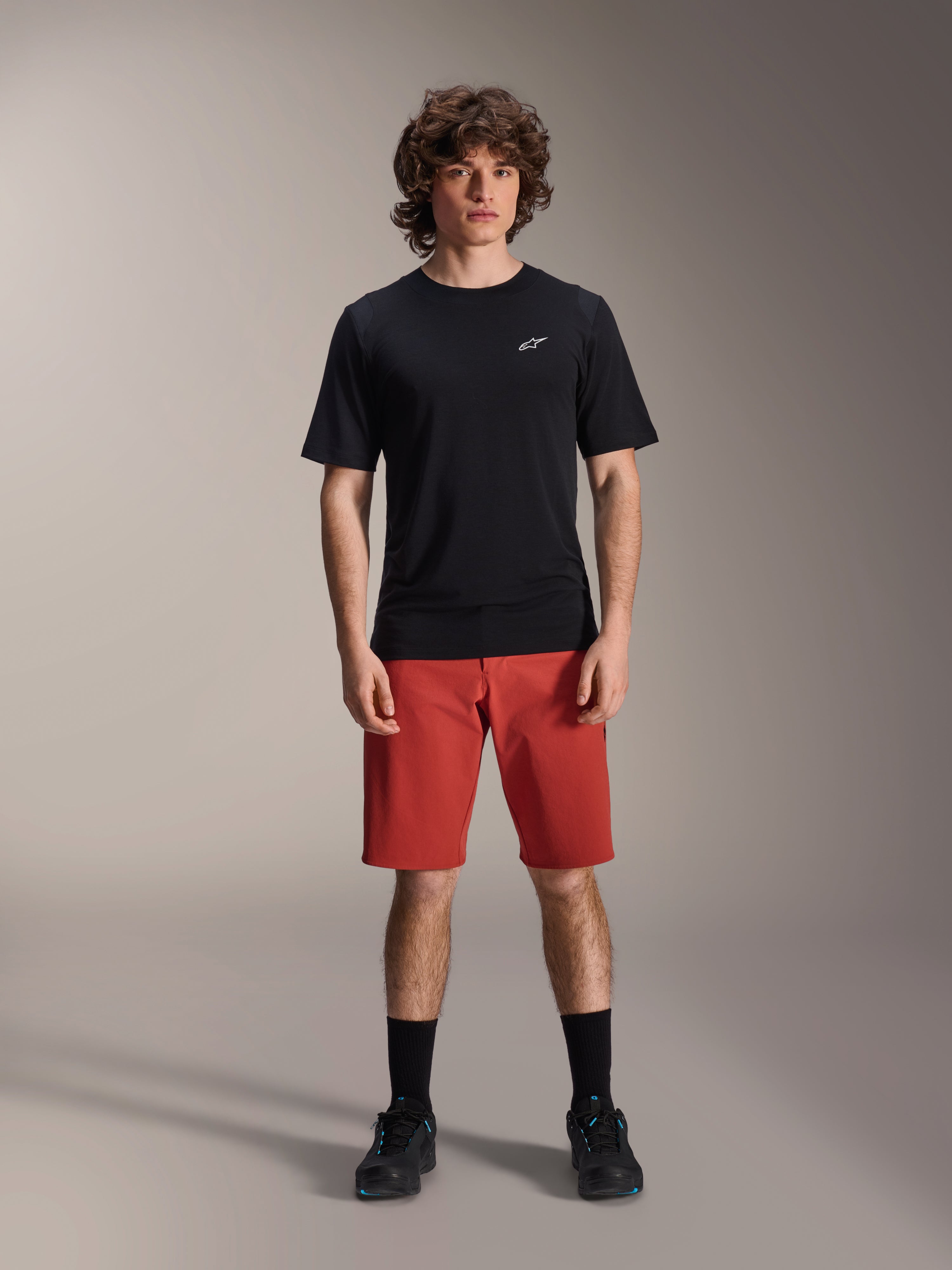 Alpinestars A-Dura Elite Shorts, pantaloncini MTB in Dark Orange, indossati con maglia nera a maniche corte e scarpe da ciclismo, abbigliamento tecnico per mountain bike