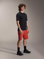 Modello uomo che indossa i pantaloncini Alpinestars A-Dura Elite in Dark Orange e la maglia a maniche corte A-Dura Dri Wool in nero, abbigliamento tecnico per mountain bike, abbinato a calze e scarpe nere, design sportivo per il ciclismo fuoristrada.