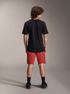 Modello che indossa i pantaloncini Alpinestars A-Dura Elite in arancione scuro e una maglia a maniche corte A-Dura Dri Wool nera, visto di spalle, abbinati a calze nere e scarpe da ciclismo, abbigliamento professionale da mountain bike