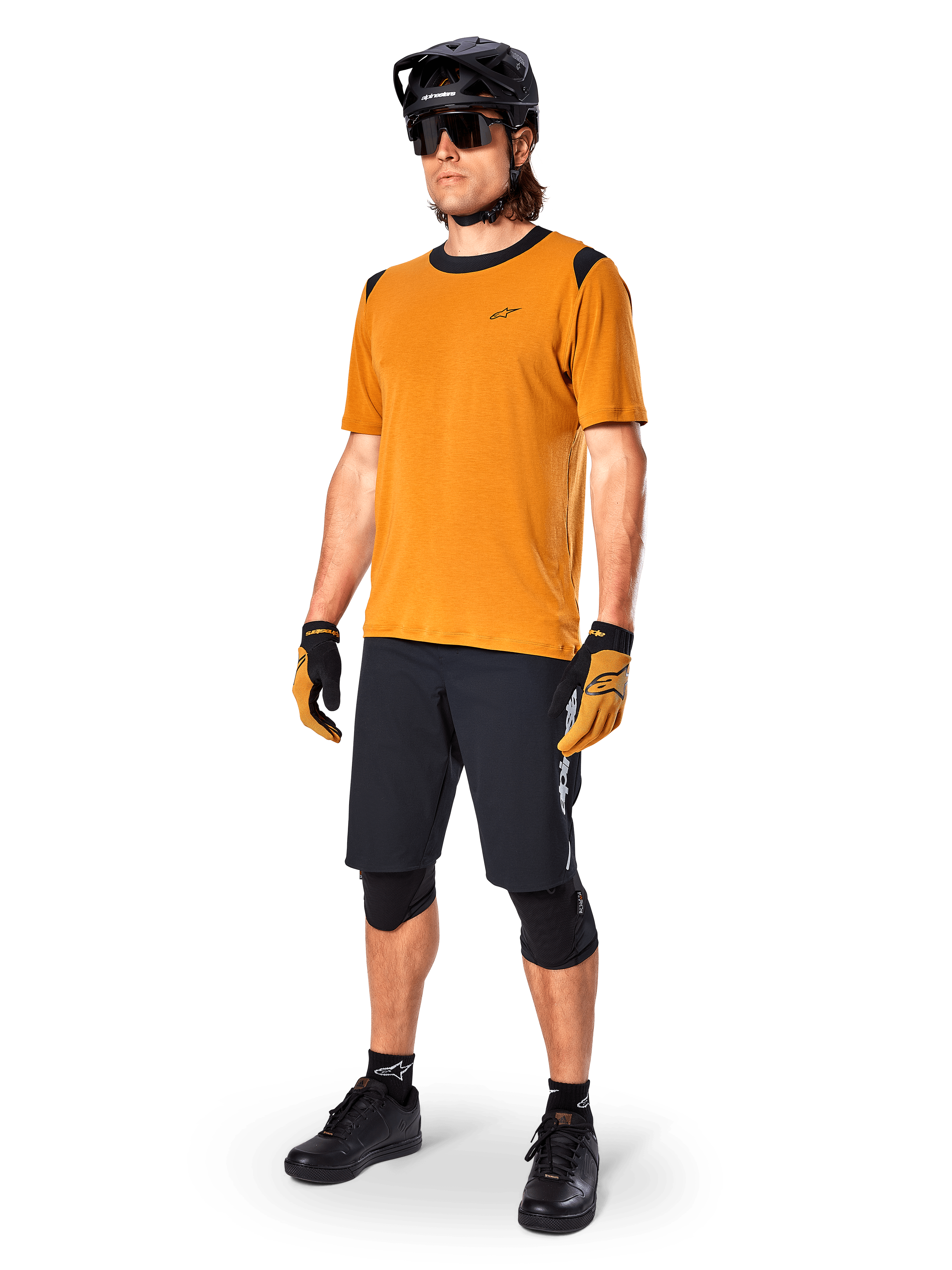 Maglia Alpinestars A-Dura Dri Wool a maniche corte in Dark Gold, maglia da mountain bike con dettagli neri su spalle e colletto, abbinata a pantaloncini da MTB neri, casco nero e occhiali da sole, abbigliamento tecnico da ciclismo fuoristrada