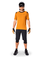 Alpinestars A-Dura Dri Wool Short Sleeve Jersey in Dark Gold, maglia da mountain bike a maniche corte, tessuto giallo senape con colletto e dettagli sulle spalle neri, indossata con pantaloncini neri e protezioni, abbigliamento tecnico da ciclismo per trail