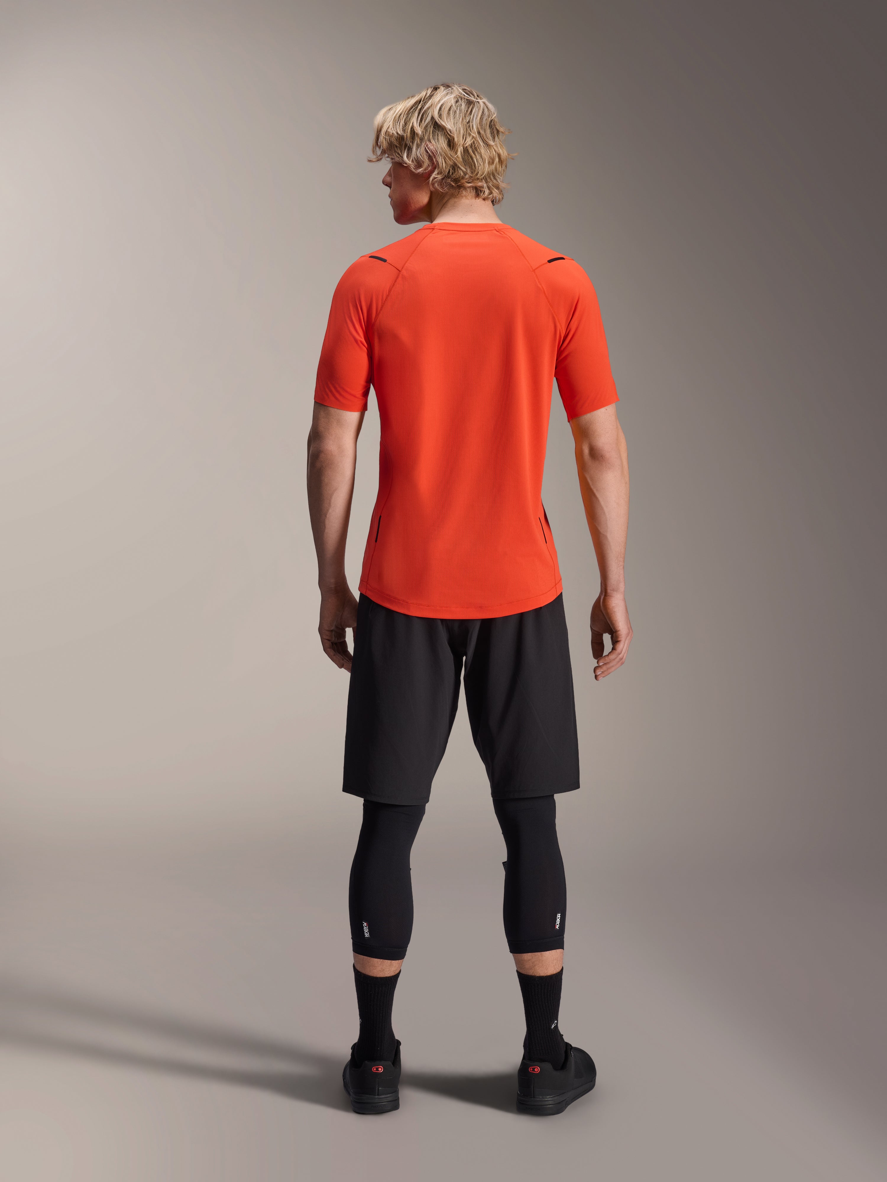 Alpinestars A-Aria Astar Jersey, maglia MTB a maniche corte, Spicy Orange, vista posteriore che mostra la vestibilità performante e la coda più lunga, abbinata a pantaloncini da ciclismo neri e leggings