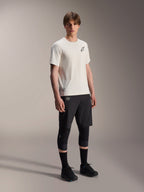 Alpinestars A-Aria Astar Jersey, a maniche corte, ecru, con logo nero sul petto, indossata con pantaloncini da ciclismo neri e ginocchiere, abbigliamento tecnico leggero per MTB