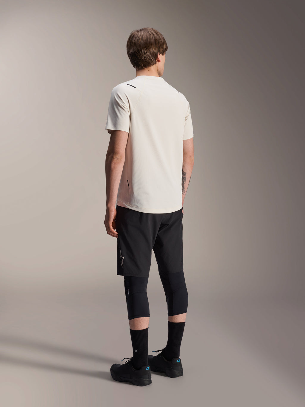 Alpinestars A-Aria Astar Jersey, maglia MTB a maniche corte, ecru, vista posteriore che mostra la vestibilità performante e la coda più lunga, abbinata a pantaloncini da mountain bike neri, protezioni per le ginocchia e scarpe da riding nere per sessioni trail off-road