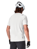 Alpinestars A-Aria Astar Jersey, maniche corte, White Dove, vista posteriore di maglia da mountain bike leggera e traspirante, indossata con casco bianco e guanti da ciclismo neri, con parte posteriore allungata per una maggiore copertura