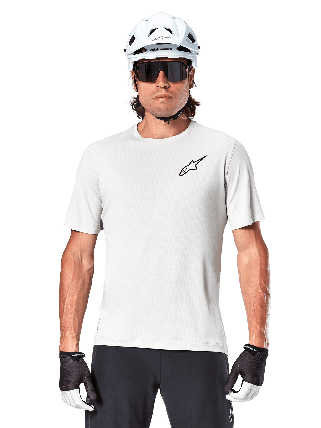 Ciclista che indossa la maglia a maniche corte Alpinestars A-Aria Astar, colore White Dove con piccolo logo Astar nero sul petto, casco da ciclismo bianco, occhiali da sole neri e guanti neri e bianchi, abbigliamento tecnico da MTB per fuoristrada