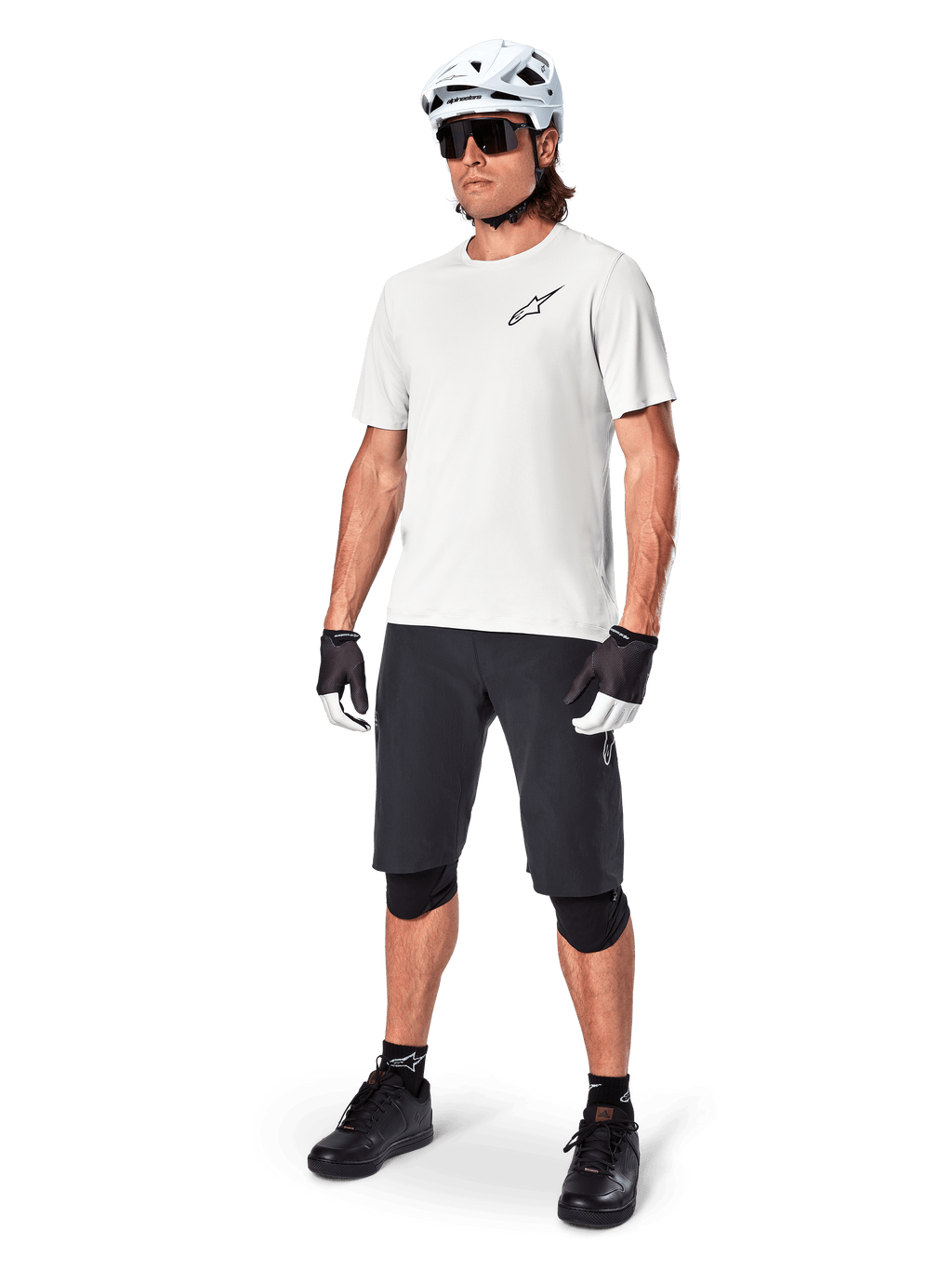 Ciclista MTB che indossa la maglia a maniche corte Alpinestars A-Aria Astar in White Dove, abbinata a pantaloncini da mountain bike neri, casco bianco e ginocchiere nere, con un piccolo logo nero sul petto, equipaggiamento tecnico coordinato per performance sui sentieri